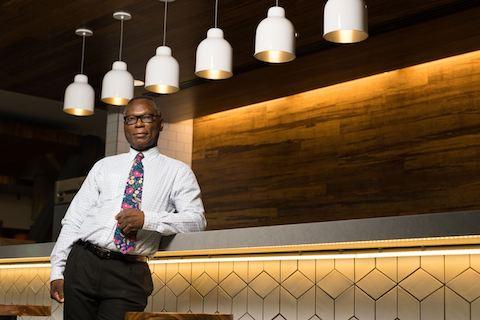 Henry Aigbedo, Ph.D., leaning on a railing in a dimly lit room.