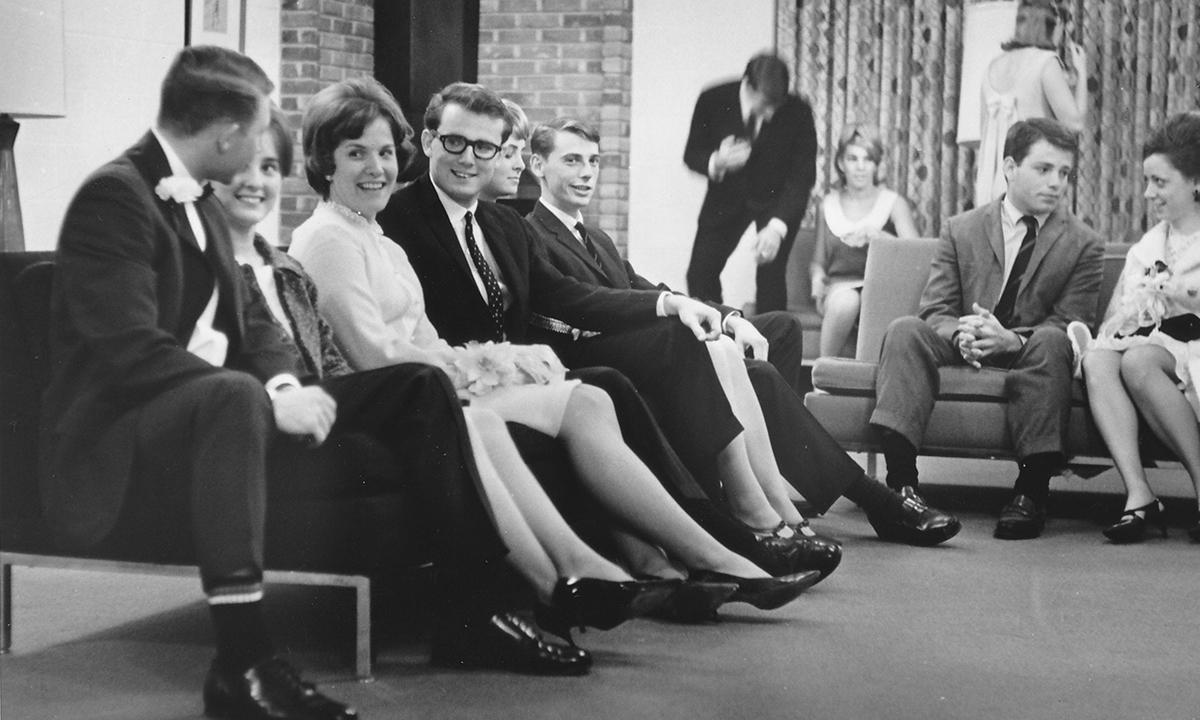 A group of people in traditional 1960's clothing sitting on a couch