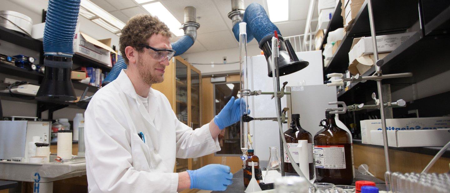 Man in goggles and lab coat works in a lab.